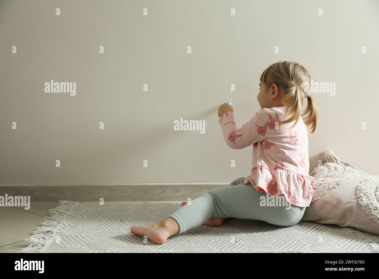 Little girl drawing on beige wall indoors, space for text. Child`s art Stock Photo